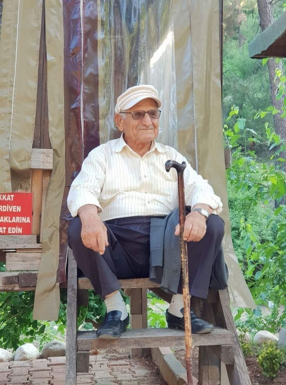Hacı Şefik Çetin, bahçede ahşap basamakta bastonuyla otururken